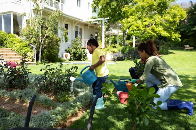 Side view of an African American boy in the garden watering plants, his parents gardening next to him. Family enjoying time at home, lifestyle concept