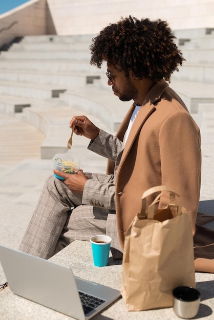 ブランチを持っているアフリカ系アメリカ人の男の側面図。サラダを食べ、仕事をしながらコーヒーを飲む男。食事、仕事のコンセプト