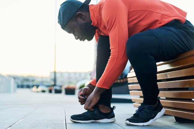 Side view of african american runner bending over sneaker while tying shoelace