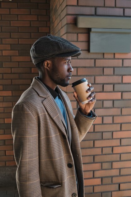 Side view of African young man drinking coffee and looking away standing in the city