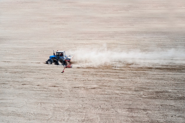 Side view of agricultural industrial tractor plows soil field for sowing , aerial view. Land cultivation.