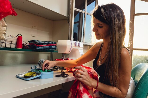 Side view of Argentinian Caucasian young woman smiling and working sitting in her sewing workshop