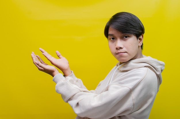 Side view of an asian man in a beige hoodie pointing his finger and opening arms to promote ads