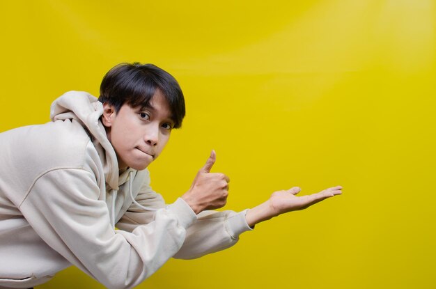 Side view of an asian man in a beige hoodie pointing his finger and opening arms to promote ads