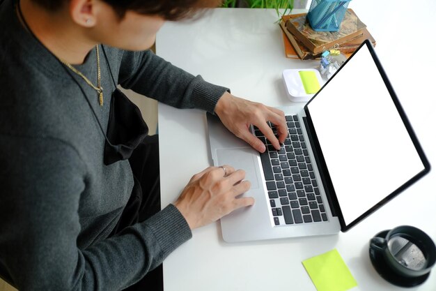 自宅から仕事中にラップトップコンピューターでオンラインで作業しているアジア人男性の側面図