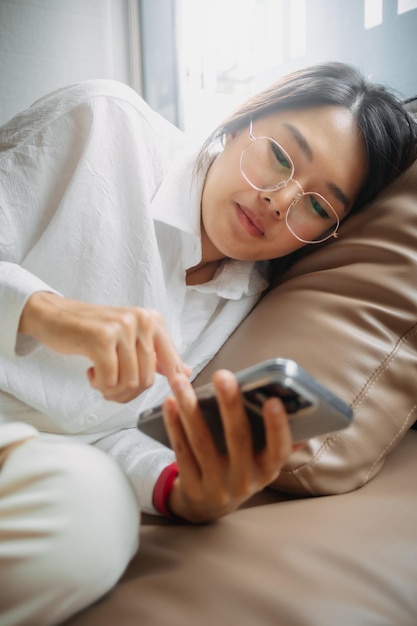 Side view of asian thai office woman using mobile phone while leaning and resting on brown couch