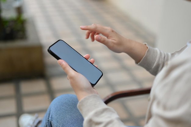 Side view of an Asian woman relaxes sitting at the backyard and using her smartphone