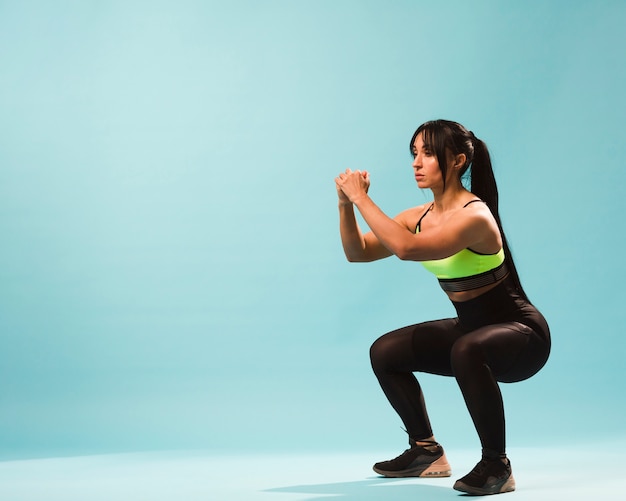 Photo side view of athletic woman in gym outfit doing squats with copy space