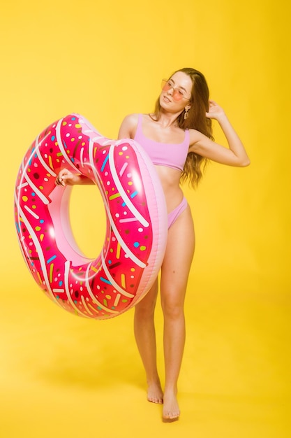 Side view of attractive young female in swimwear trendy sunglasses holding donutshaped swim ring