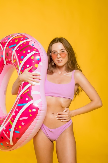 Side view of attractive young female in swimwear trendy sunglasses holding donutshaped swim ring