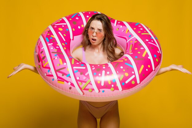 Side view of attractive young female in swimwear trendy sunglasses holding donutshaped swim ring