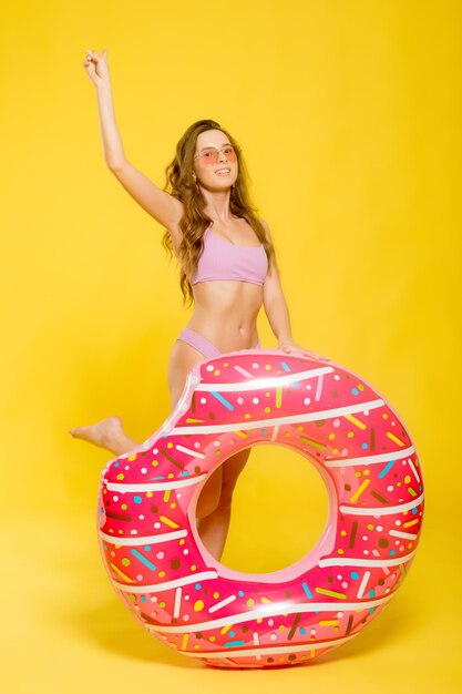 Side view of attractive young female in swimwear trendy sunglasses holding donutshaped swim ring