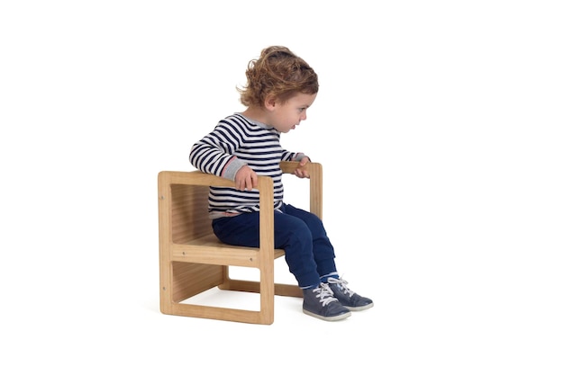 Side view of a baby boy sitting on chair and looking down on white background