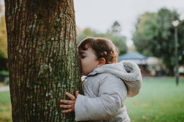 Foto vista laterale di una bambina che bacia il tronco di un albero