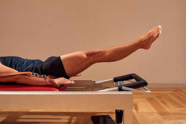 Side view of barefoot male athlete lying on pilates reformer and performing abs exercise during fitness workout Pilates man concept