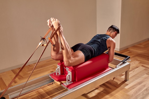 Вид сбоку на босоногого спортсмена, лежащего на реформаторе пилатеса и выполняющего упражнения на пресс во время фитнес-тренировки Концепция человека пилатеса