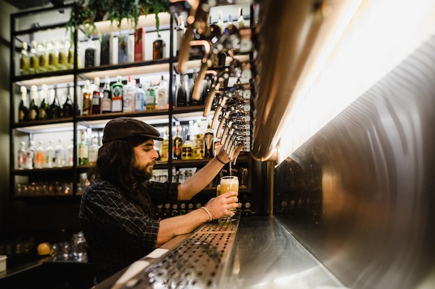 Боковой вид бармена, заполняющего пивный стакан в баре