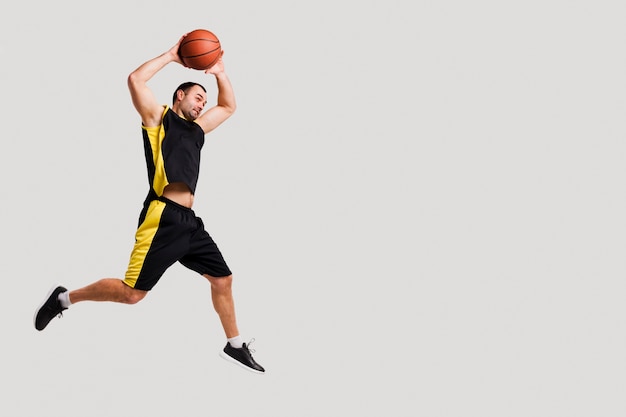 Photo side view of basketball player posing mid-air while throwing ball with copy space