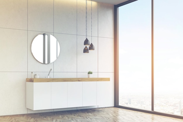 Side view of a bathroom sink with round mirror on tiled wall toned