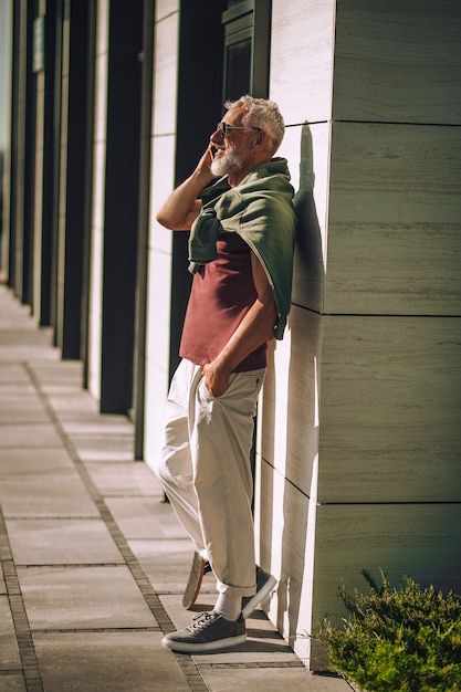 Side view of a bearded gray-haired Caucasian male in sunglasses smiling during the phone conversation