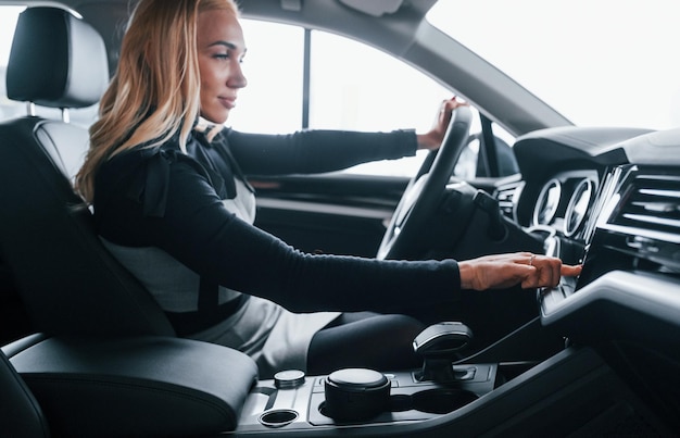 Side view of beautiful blonde in elegant clothes that sitting inside of modern car