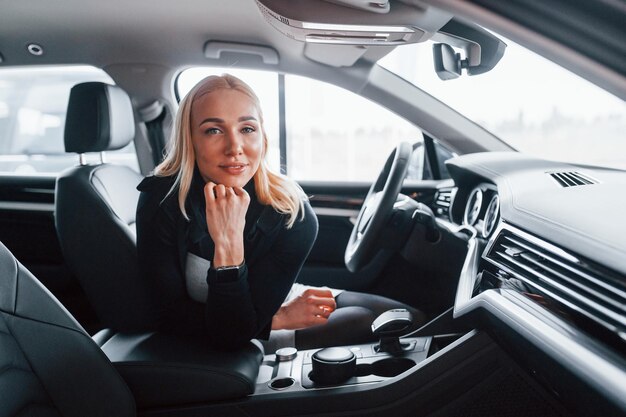 Side view of beautiful blonde in elegant clothes that sitting inside of modern car