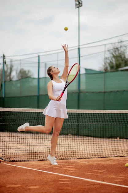 Vista laterale di una donna bella e competitiva sorridente, mentre si tiene la racchetta da tennis