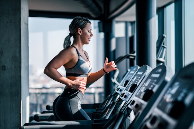 Side view of beautiful muscular woman running on treadmill.