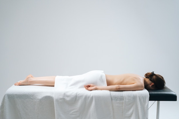 Side view of beauty young woman lying down in spa massage table on white background. Concept of massage spa treatments