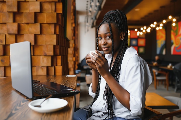 Side view of black lady enjoying morning coffee and checking emails on laptop cafe interior empty space