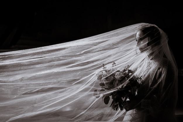 Side view of black and white photo of the bride with a bouquet in her hands and a long veil