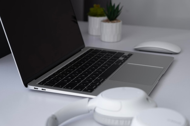 Photo side view on a blank screen laptop with mouse headphones and plants on a white table at home office