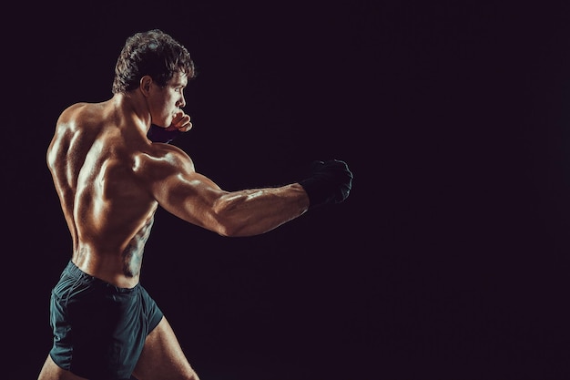 Side view of boxer in red gloves who practicing swing on black background sport concept