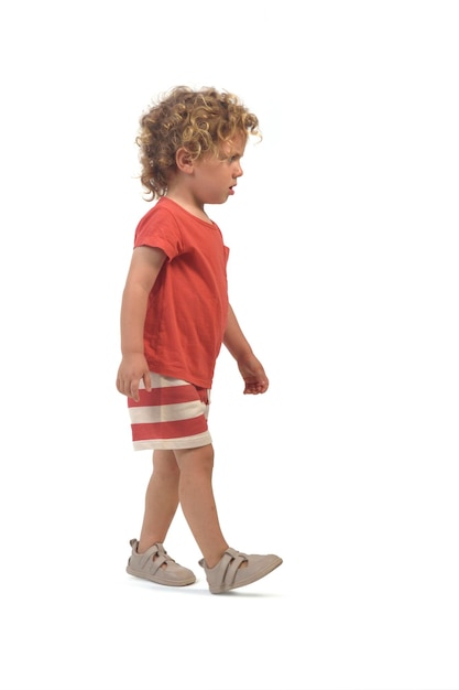 side view of a boy dressed in summer clothes walking on white background 3 year old