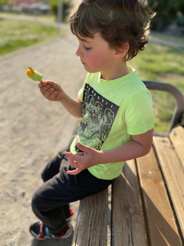 Photo side view of boy eating an ice cream at the park