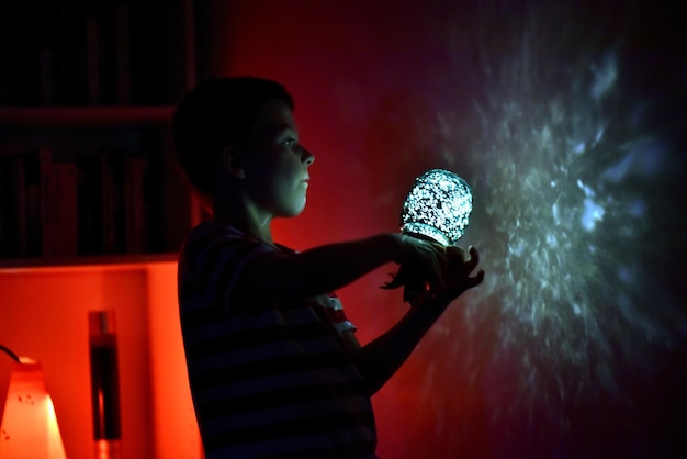 Foto vista laterale di un ragazzo che tiene l'attrezzatura di illuminazione vicino alla parete