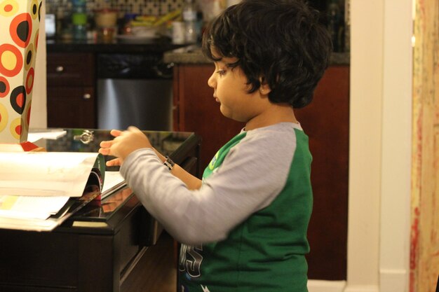 Photo side view of boy reading book on table at home