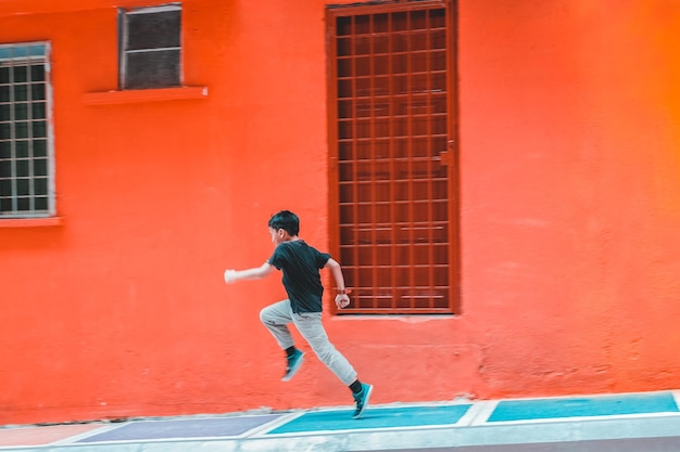 Vista laterale di un ragazzo che corre vicino a un edificio rosso