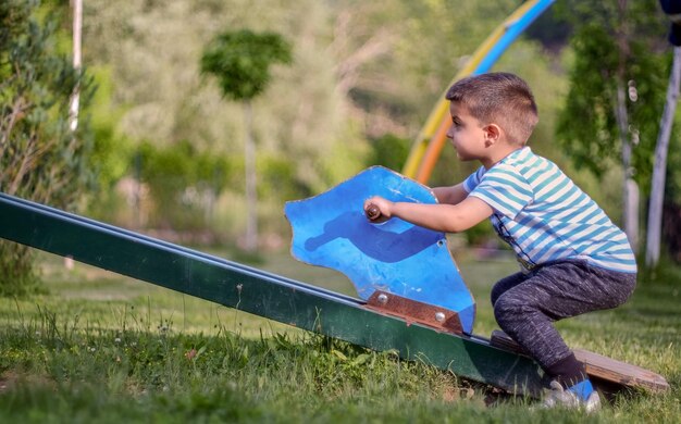 Photo side view of boy sitting on see saw in playground