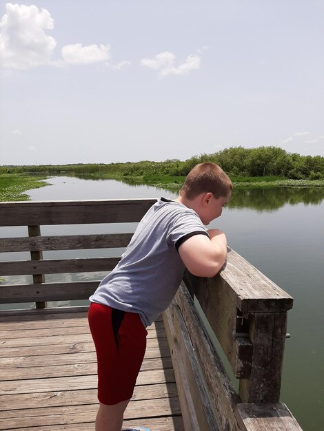 Foto vista laterale di un ragazzo in piedi vicino al lago contro il cielo