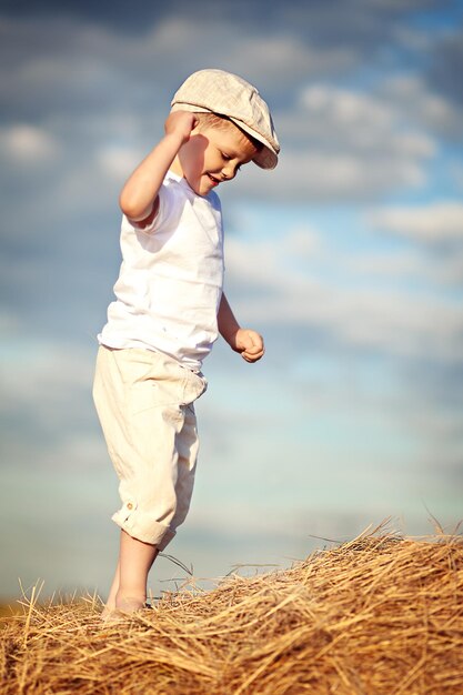 Side view of boy standing on hay against sky