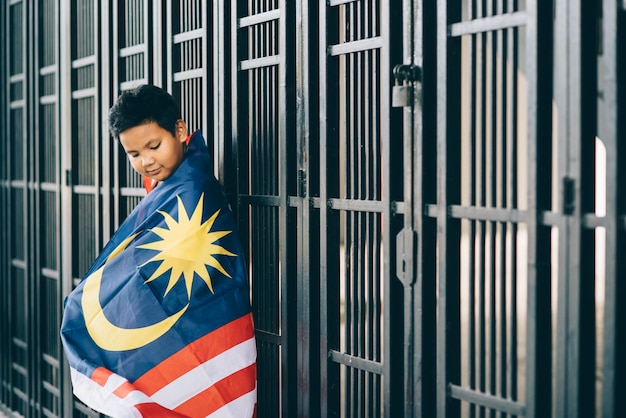 Photo side view of boy wearing malaysian flag by fence