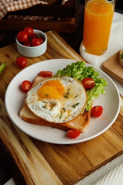 布にオレンジジュースと木製の背景にパンのスライスの箱とまな板のプレートの乾燥パンスライスに目玉焼きレタストマトをセットした朝食の側面図