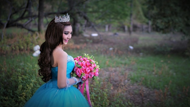 Foto vista laterale della sposa che tiene un bouquet in piedi al parco