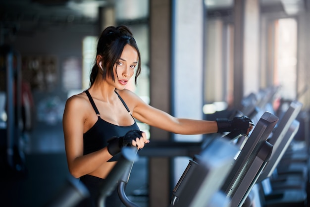 Side view of brunette woman in sportswear and wireless headphones doing cardio workout on orbitrek