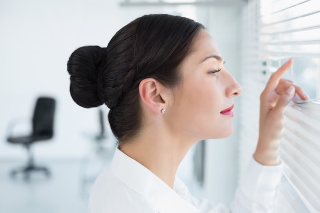 Side view of a business woman peeking through blinds at office