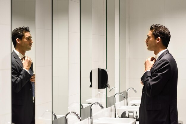 Photo side view of businessman adjusting tie in restroom