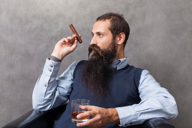 Side view of businessman in blue vest with whiskey and cigar