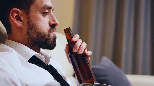 Vista laterale dell'uomo d'affari che beve birra dopo il lavoro nel suo appartamento.