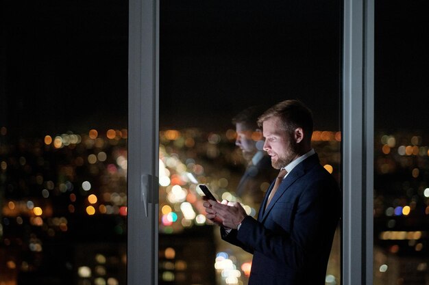 Side view of businessman scrolling in mobile phone against large window